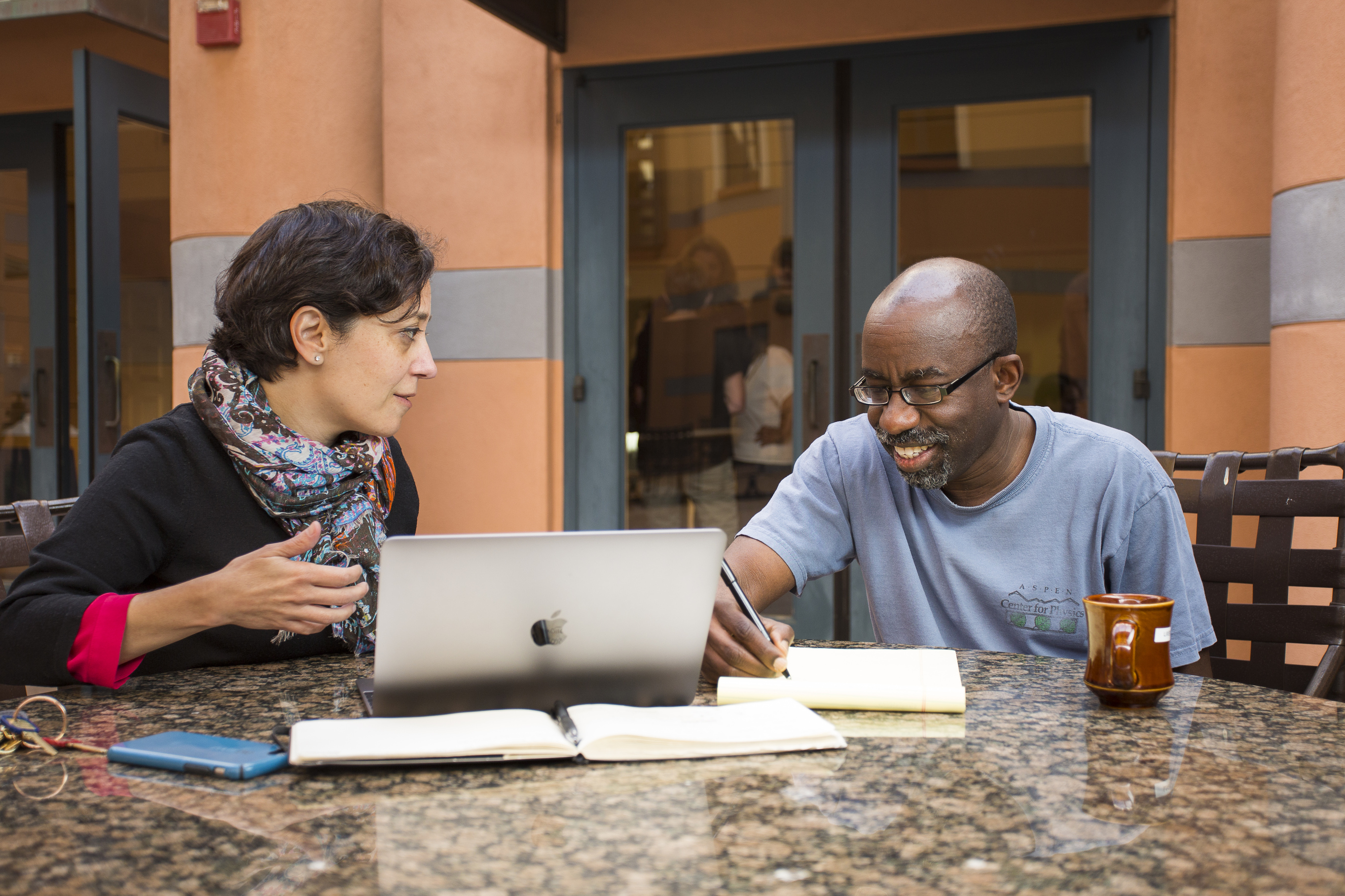 Two people discussing work on a table over a laptop and a notebook